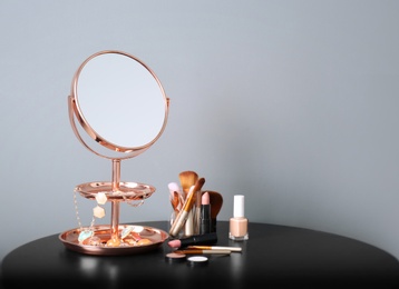 Modern mirror with makeup products and accessories on table near color wall