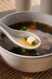 Delicious miso soup with tofu in spoon above bowl, closeup