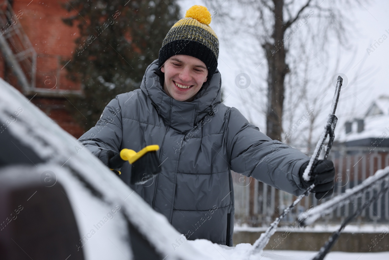 Photo of Man cleaning snow from car with brush outdoors