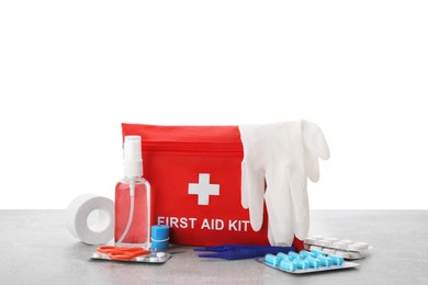 Photo of First aid kit, scissors, gloves, pills, plastic forceps and elastic bandage on light grey table against white background