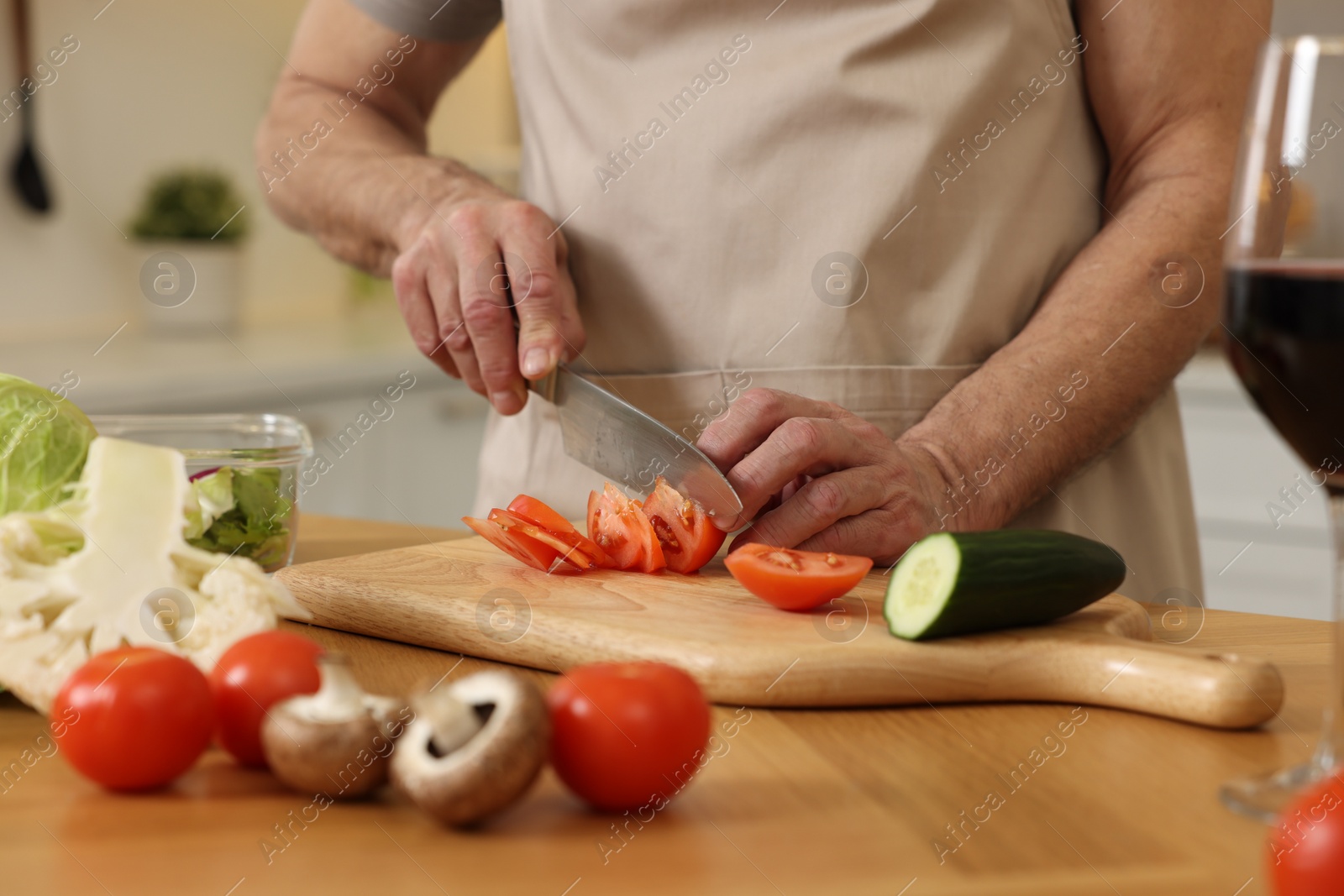 Photo of Man cutting tomato at wooden table in kitchen, closeup