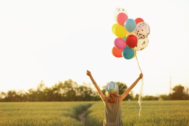 Young woman with colorful balloons in field on sunny day