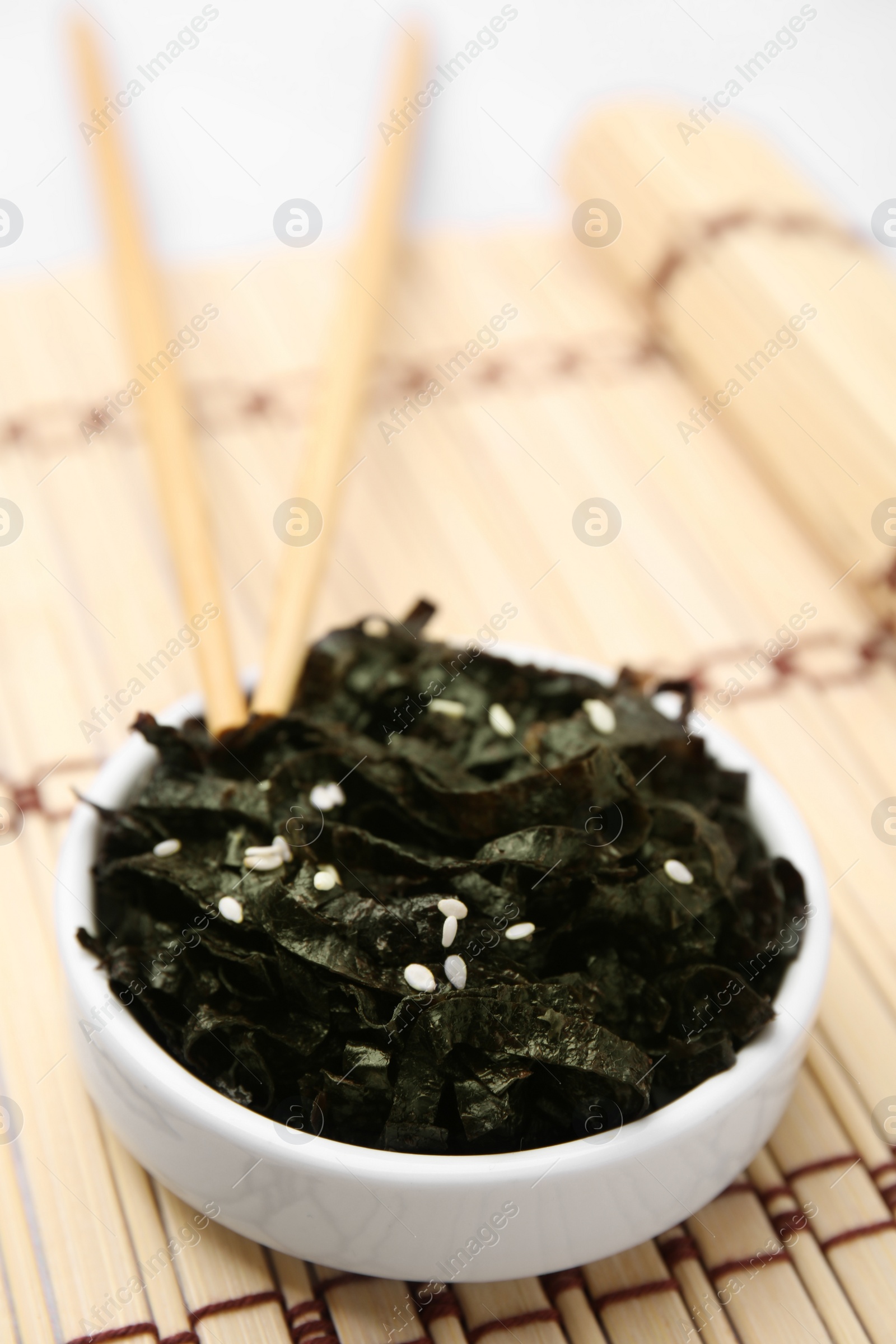 Photo of Chopped nori sheets with sesame and chopsticks on bamboo mat, closeup