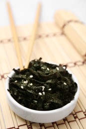 Chopped nori sheets with sesame and chopsticks on bamboo mat, closeup