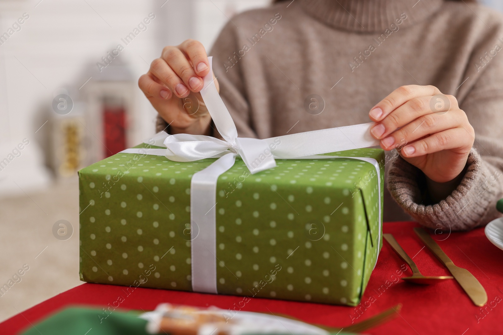 Photo of Woman opening gift box at table indoors, selective focus