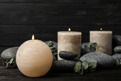 Photo of Composition with burning candles, spa stones and eucalyptus on dark wooden table