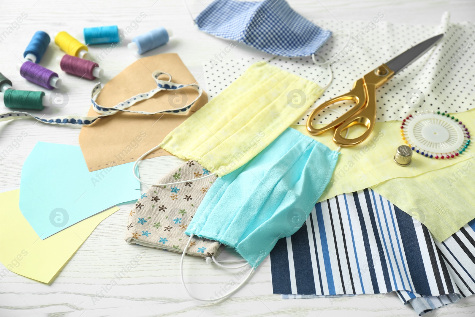 Photo of Fabric, sewing accessories and cloth masks on white wooden table. Personal protective equipment during COVID-19 pandemic