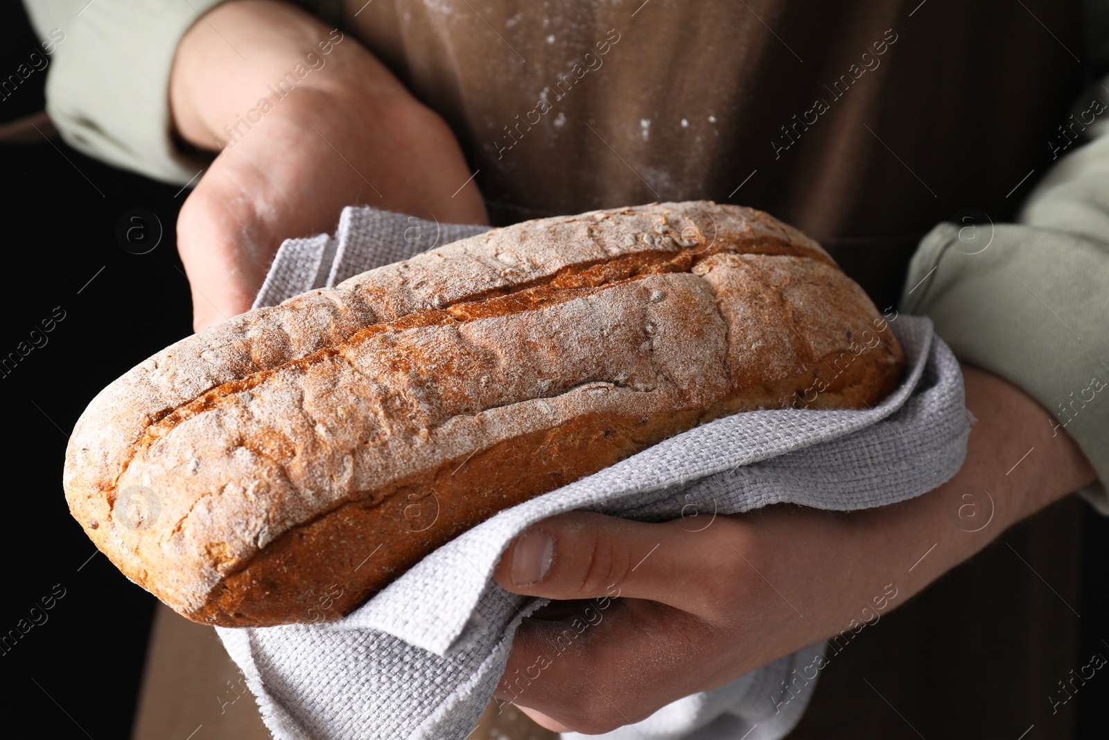 Photo of Woman holding freshly baked bread on black background, closeup