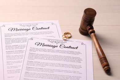 Photo of Marriage contracts, gold rings and gavel on light wooden table, closeup