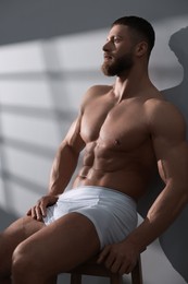 Photo of Young man in stylish white underwear sitting on chair near grey wall