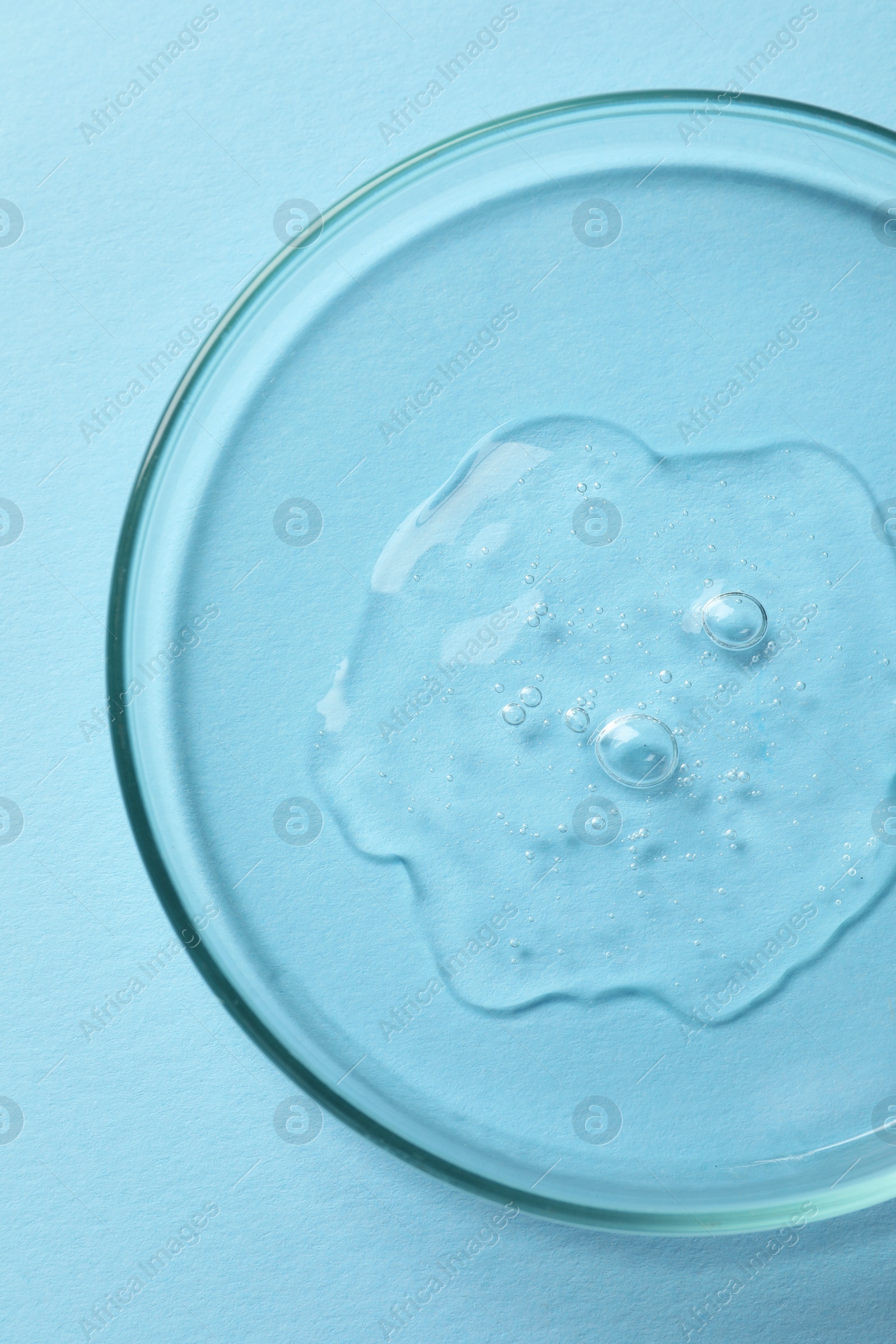 Photo of Petri dish with sample of cosmetic oil on light blue background, top view