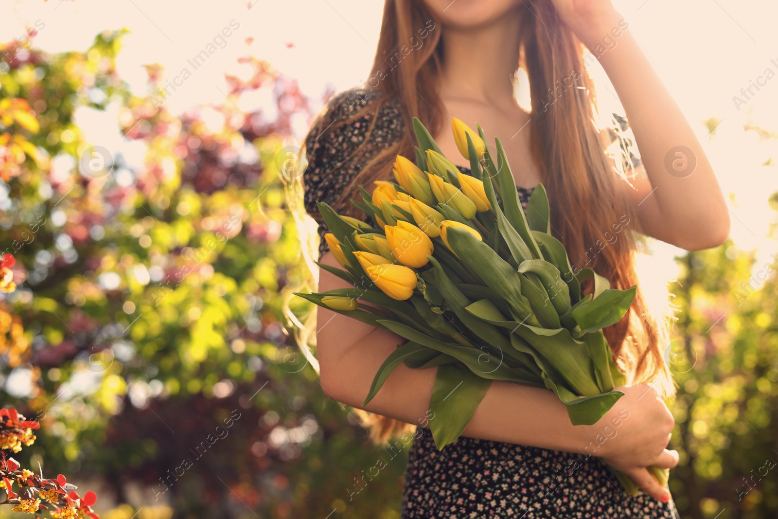 Photo of Teenage girl with bouquet of yellow tulips in park on sunny day, closeup. Space for text