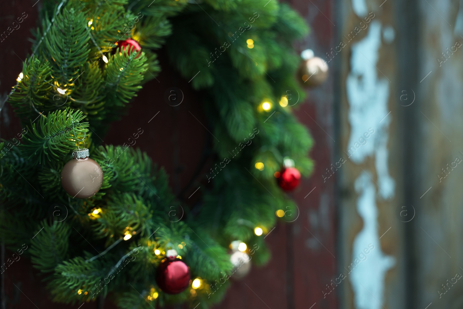 Photo of Beautiful Christmas wreath with baubles and string lights hanging on wall, closeup. Space for text