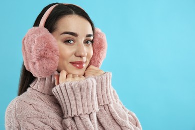 Photo of Beautiful young woman wearing earmuffs on light blue background. Space for text