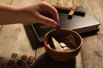 Photo of Donate and give concept. Woman putting coin into bowl with money at wooden table, closeup