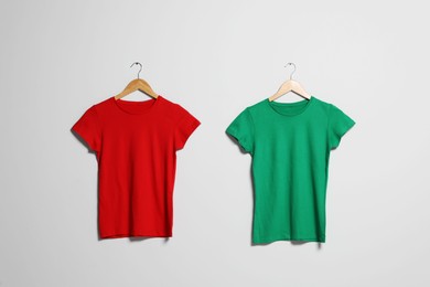 Photo of Hangers with different t-shirts on light wall. Mockup for design