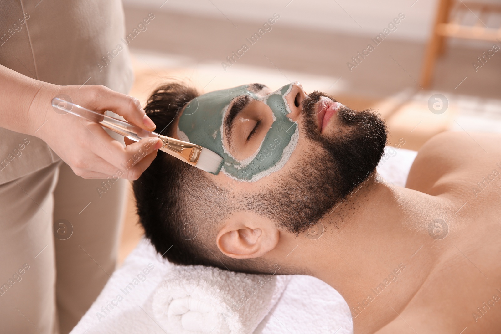 Photo of Cosmetologist applying mask on man's face in spa salon