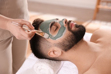 Cosmetologist applying mask on man's face in spa salon