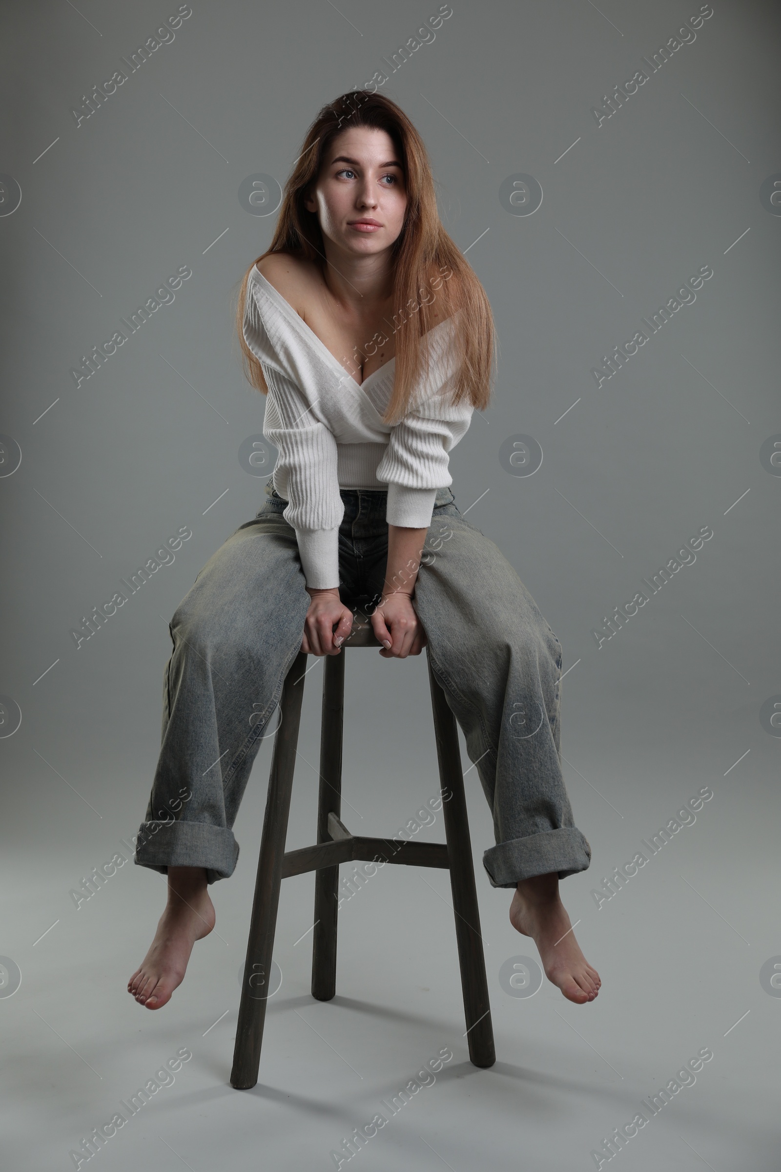 Photo of Beautiful young woman sitting on stool against grey background