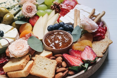 Photo of Wooden plate full of assorted appetizers on table, closeup