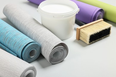 Different wallpaper rolls, brush and bucket with glue on light background