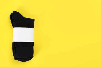 Photo of Pair of black cotton socks on yellow background, top view. Space for text