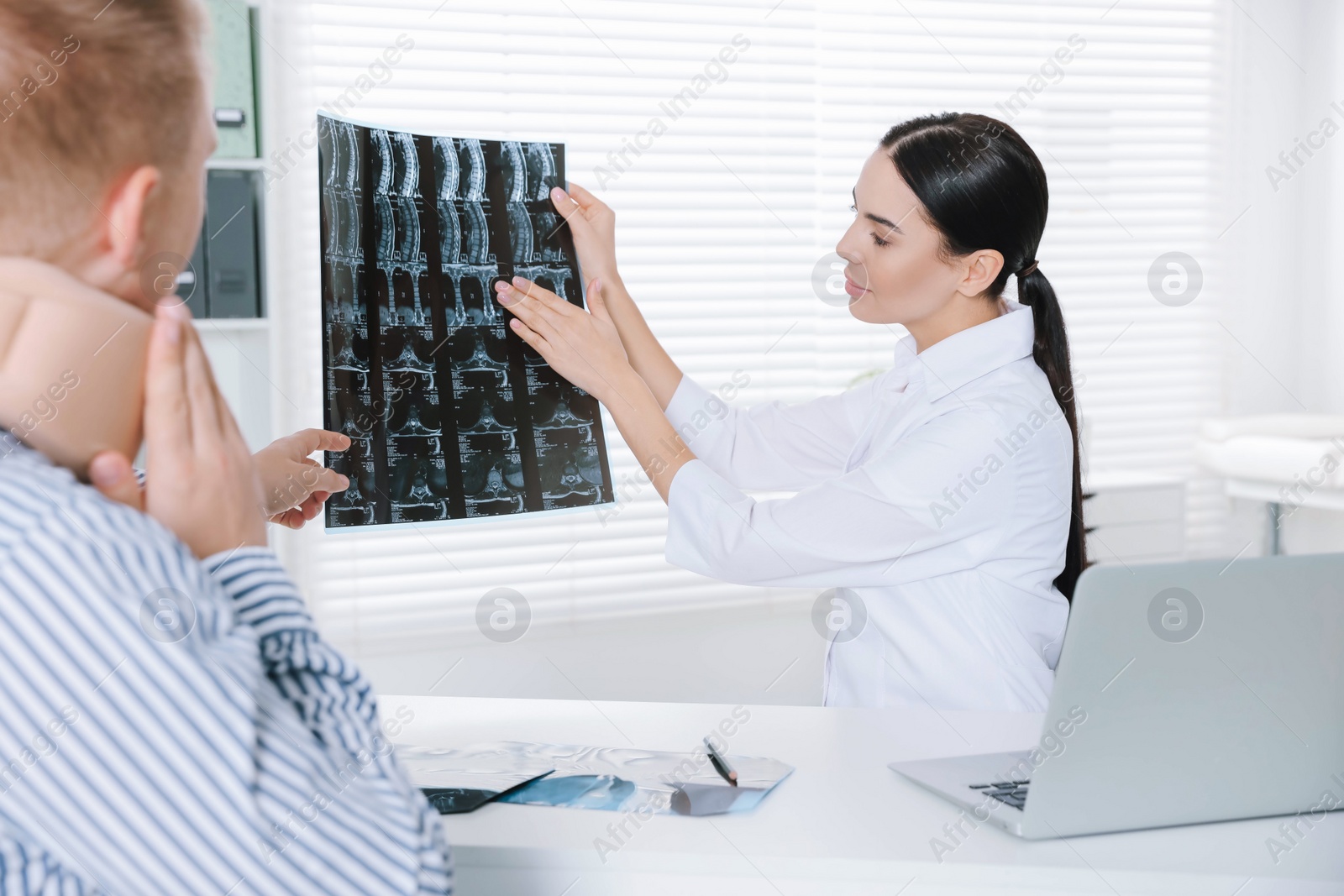 Photo of Doctor with neck MRI image consulting patient in clinic