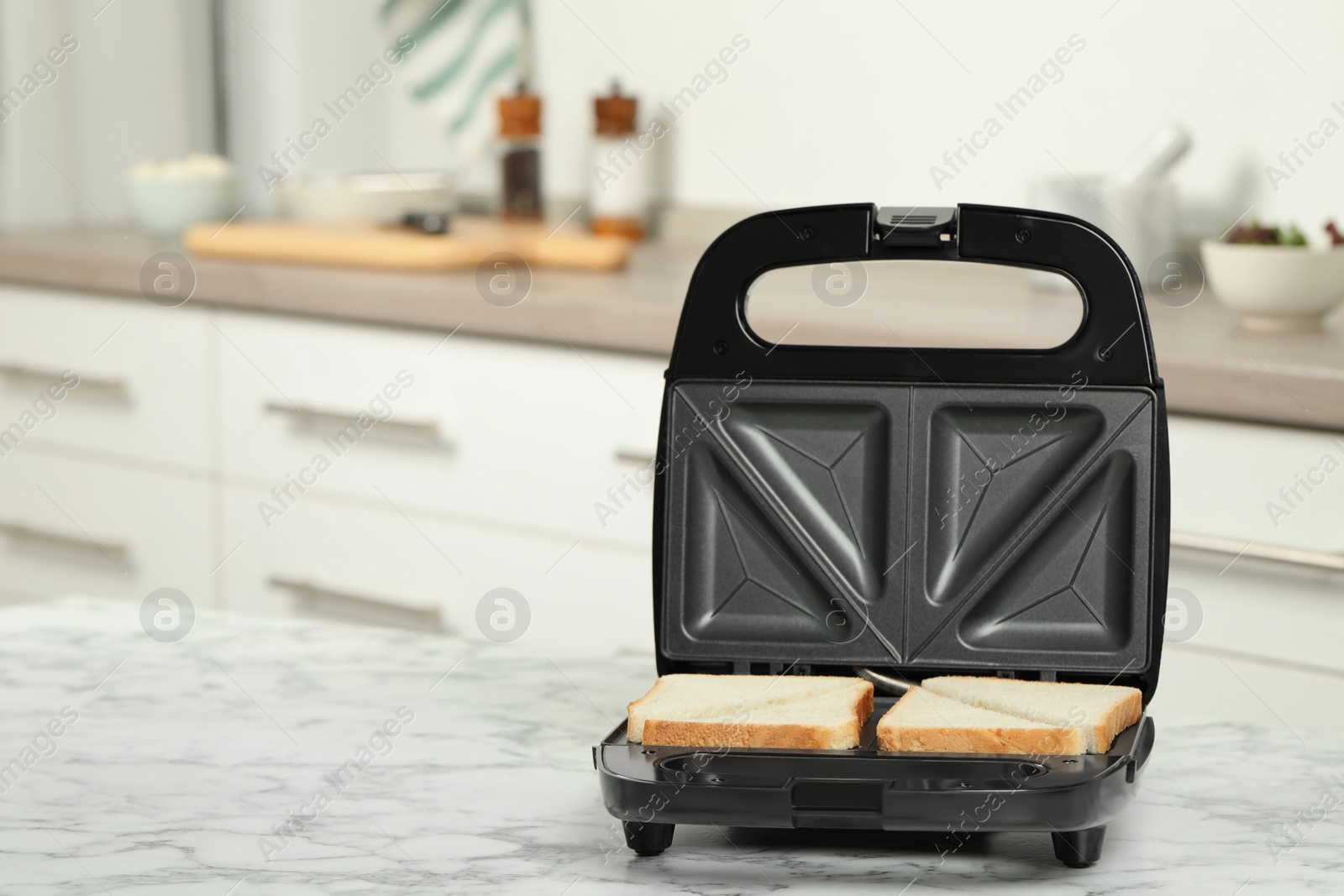 Photo of Modern sandwich maker with bread slices on white marble table in kitchen, space for text