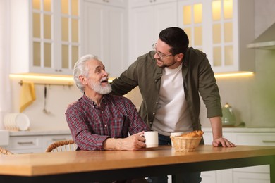 Happy son and his dad at wooden table in kitchen