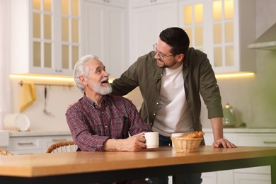 Photo of Happy son and his dad at wooden table in kitchen