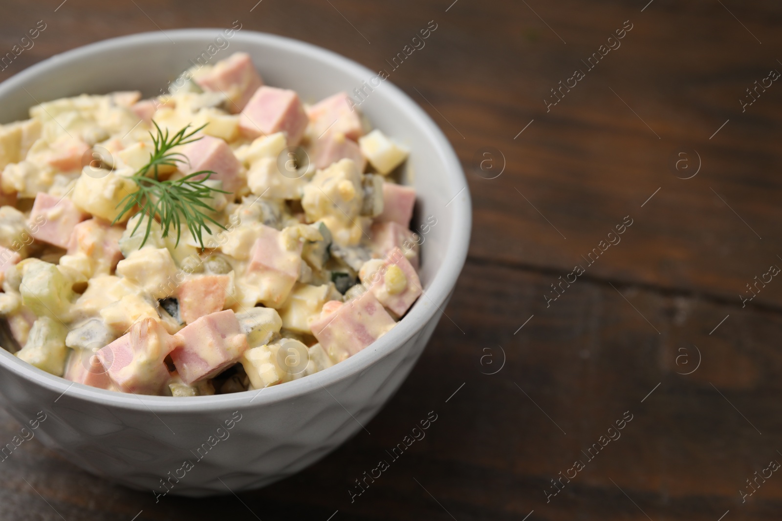 Photo of Tasty Olivier salad with boiled sausage in bowl on wooden table, closeup. Space for text