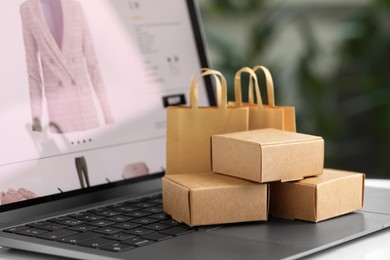 Photo of Online store. Small parcels and shopping bags on laptop, closeup