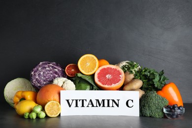 Photo of Different products and card with phrase VITAMIN C on black table