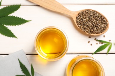 Photo of Hemp oil, fresh leaves and seeds on white wooden table, flat lay