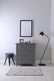 Photo of Elegant room interior with stylish chest of drawers, pouf and floor lamp