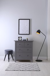 Elegant room interior with stylish chest of drawers, pouf and floor lamp