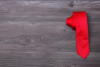 Stylish red silk necktie on dark grey wooden table, top view with space for text