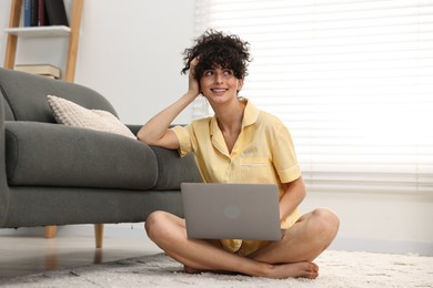 Photo of Beautiful young woman in stylish pyjama with laptop on floor at home