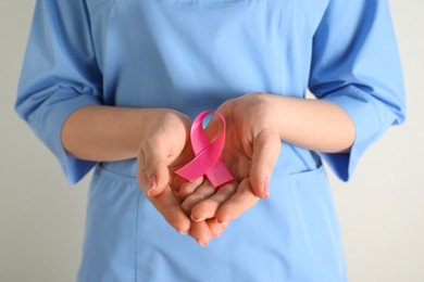 Mammologist with pink ribbon on light background, closeup. Breast cancer awareness