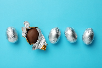 Chocolate eggs wrapped in foil on light blue background, flat lay