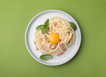 Photo of Delicious pasta Carbonara with egg yolk on light green background, top view