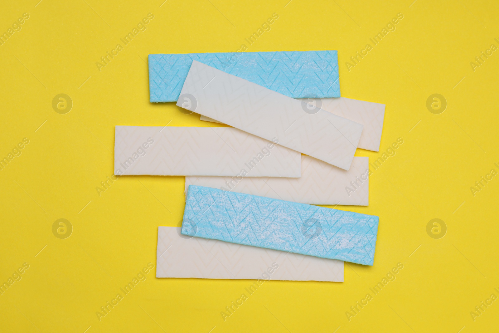 Photo of Sticks of tasty chewing gum on yellow background, flat lay