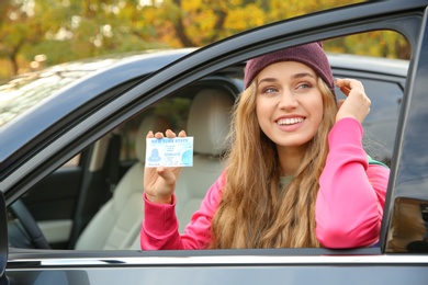 Photo of Young woman holding driving license near open car