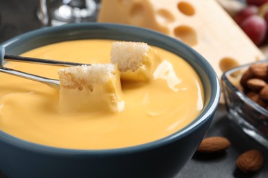 Pot of tasty cheese fondue and forks with bread pieces on grey table, closeup