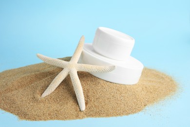 Photo of Jars with cream and starfish on sand against light blue background. Cosmetic products