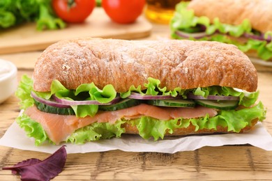 Delicious sandwich with fresh vegetables and salmon on wooden table, closeup