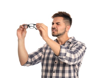 Young man with vision problems holding glasses on white background
