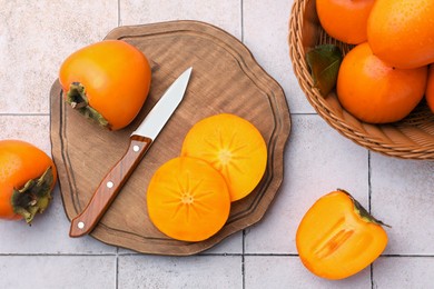 Delicious ripe juicy persimmons and knife on tiled surface, flat lay