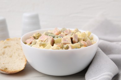 Photo of Tasty Olivier salad with boiled sausage in bowl and bread on white table, closeup