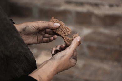 Poor homeless with piece of bread outdoors, closeup